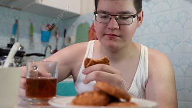 breakfast, food and people concept - happy young woman with cup of tea eating chocolate chip cookie at home over kitchen