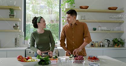 Diverse couple prepping salad chopping cucumber and carrots at kitchen island sorting ingredients