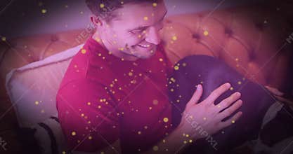 Man holding dog on lap and lifting paws onto couch cushion while demonstrating pet health care