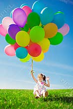 Little girl holding colorful balloons. Child playing on a green