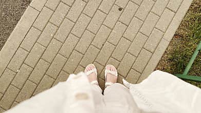 Top-down view of a person in white attire and sandals walking on a tiled path in strong wind.
