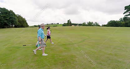 Male and female golf players walking with clubs and entering golf course, copy space