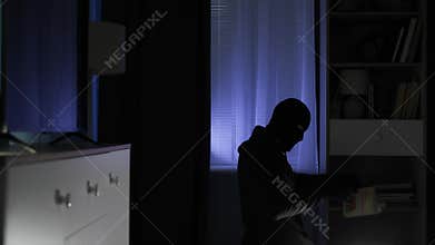 house guard, adult man in balaclava and rummaging through things in search of valuable things and money in the apartment