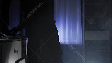 thief, an adult male in black clothes and a balaclava, rummages through other people's things in search of valuables