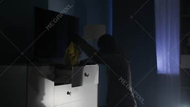 Trespassing, dangerous man in balaclava rummages through chest of drawers in search of money and jewelry at night