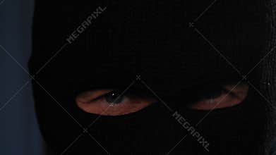 concept of robber and criminal, suspicious man in balaclava looking around in dark room, close-up