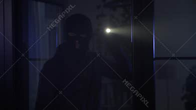 robbery, male thief in balaclava with flashlight in hands inspects the premises in search of valuables at night