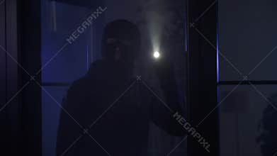 burglary, adult male in black clothes and balaclava with flashlight in hand enters room looks around at night