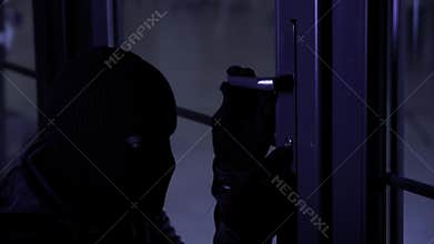dangerous man in balaclava in gloves with picklocks tries to pick the lock and open door to room at night
