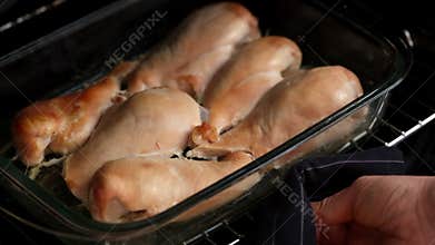 Woman hand pulling glass baking tray with baked chicken breasts out of an oven