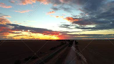 Drone timelapse of a road in expansive rural fields under dramatic sunset sky with colorful clouds