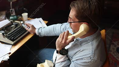 Male author at vintage desk talking on wired phone, typewriter and papers in cinematic