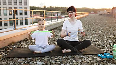 Mother and daughter exercising with resistance bands during sunset outdoors