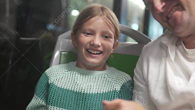 A little girl and her dad are traveling in the evening in a city bus and are playing a game of rock, paper, and scissors