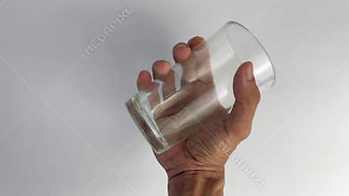Close-up of slow hand shaking of a clear glass on a white background
