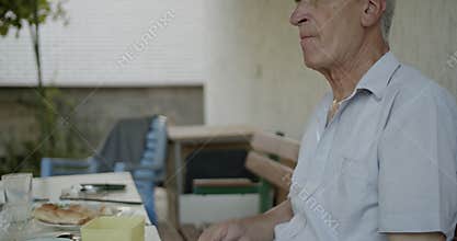 Elderly Man Blowing His Nose While Having Breakfast Outdoors: A Touching Portrait of Senior Life, Allergies, or a Common Cold