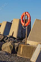 An orange lifebuoy mounted on a pole amongst the concrete blocks on a breakwater.