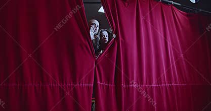 Young Actors Peek Through Red Stage Curtains, Excited and Ready for Their Performance