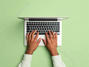A person typing on a white MacBook with black keys against a light green backdrop, in a minimalist flat lay composition - AI