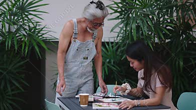 Experienced Senior Artist Mentoring Young Aspiring Painter Sharing Watercolor Techniques on a Wooden Table