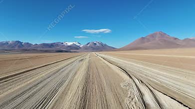 Drone glides over Bolivia desert dunes with tracks and distant hills