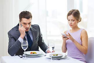 Busy couple with smartphones at restaurant