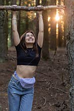 Happy young woman doing pull-ups on a tree branch in the forest
