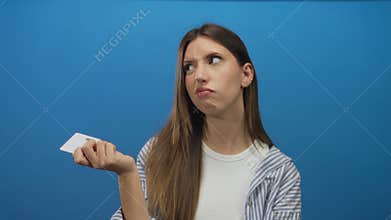 Young hispanic woman holding white plastic card with finger on chin against blue background in studio; uncertainty