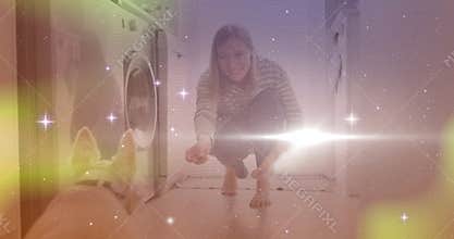 Woman crouching by washer offering treat on floor, luring dog under sparkle overlay pet training