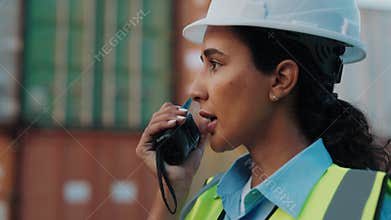 Side View of the Latino Woman in White Helmet Walking Outside at the Construction Site and Using Walkie Talkie.