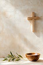 Wooden cross on textured wall with olive branch and wooden bowl in gentle sunlight