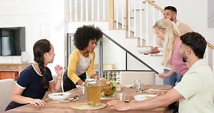 Friends enjoying meal together, serving food and chatting around dining table
