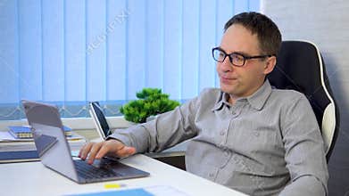 a businessman works in a bright office during the day. young man in eyeglasses with laptop and looking extremely