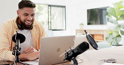 Smiling man using laptop and microphone for podcasting in home office