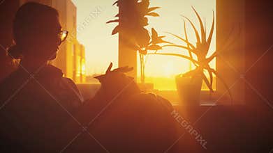 black dark silhouette lady sits in chair by window, woman with cat in hands strokes pet animal with love care. Cozy dark