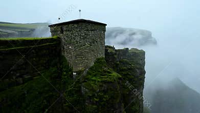 A mysterious stone tower on the foggy mossy cliff.