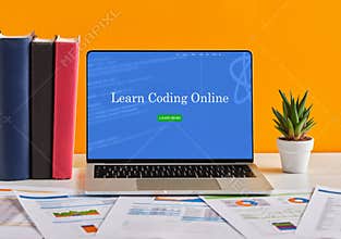 Laptop displaying learn coding online website on work desk with books and documents