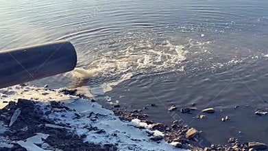 dumping dirty water into a winter lake. a sewer pipe with a turbid flow