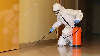 Person in protective suit spraying substance from tank on floor