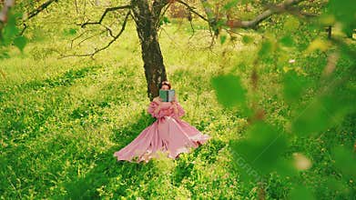 Retro woman sitting under tree reading paper book. Summer garden green grass