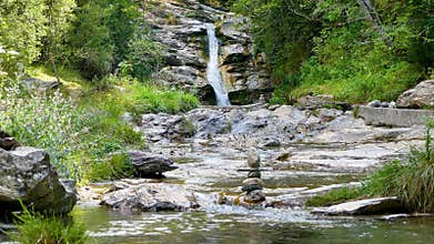 Stacked stones in a mountain stream with a small waterfall in the background.