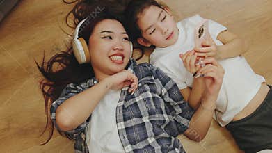 A relaxed family scene as a mother and daughter lie on the floor, each enjoying their own activities—music on
