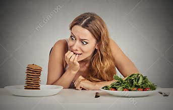 Woman deciding whether to eat healthy food or sweet cookies she craving
