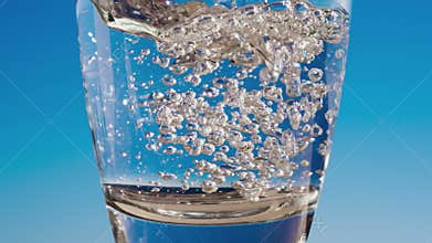 Blue water is flowing into the glass forming bubbles and splashes