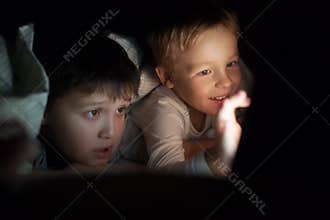 Two boys watching movie or cartoon on pad at night