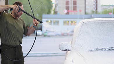 A middle aged man meticulously washes his blue car at a self-service car wash.