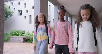 Diverse female preteens entering campus corridor holding hands walking to courtyard with backpacks