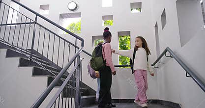 Diverse female kids descending stairs at school, third joining landing, holding backpacks together