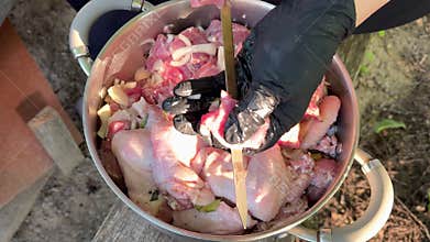 Hands in black gloves threading marinated pork and chicken wings onto metal skewers for barbecue grilling with onions