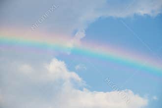 Bright pastel rainbow arching across blue sky with soft white cloud creating calm optimistic mood